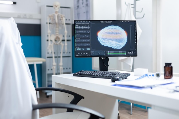 Computer with mri brain on screen standing on table in empty examination office ready for oncology consultation. Hospital room equipped with professional medical tools. Tomography image