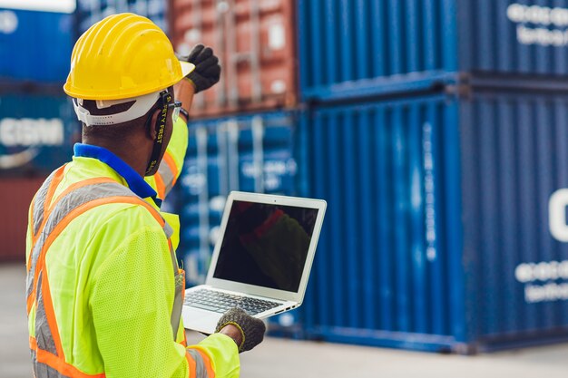 Computerlaptop leeg scherm met achteraanzicht van voorman stafmedewerker die in logistieke controle werkt en containers bij havenvracht laadt naar vrachtwagens voor export- en importgoederen.