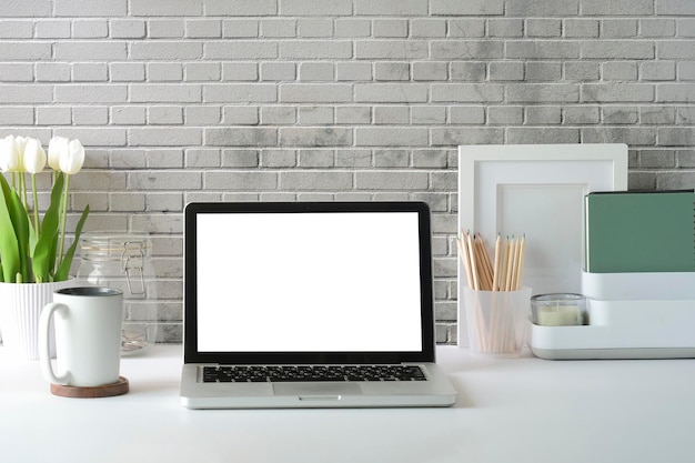 Computerlaptop met leeg scherm bloempot koffiekopje en fotolijstje op witte tafel