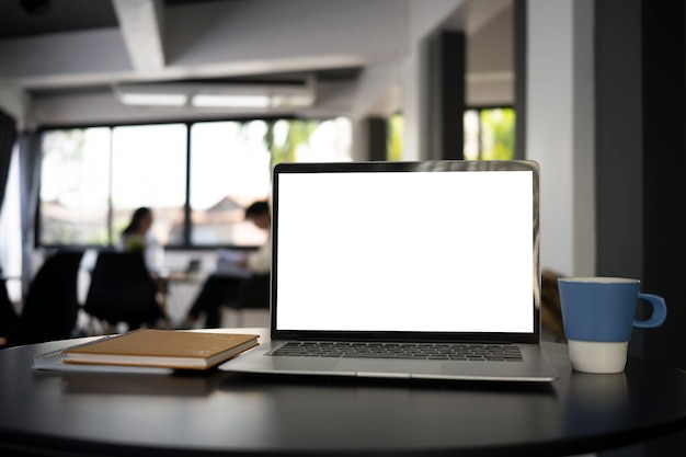 Computerlaptop met leeg scherm, koffiekop en notitieboekje op zwart bureau.