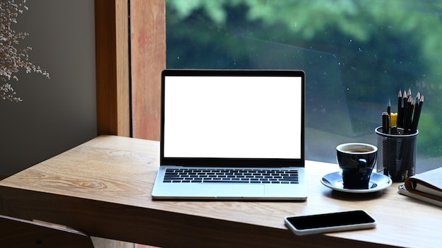 Computerlaptop, slimme telefoonboeken en koffiekopje op houten tafel bij het raam.