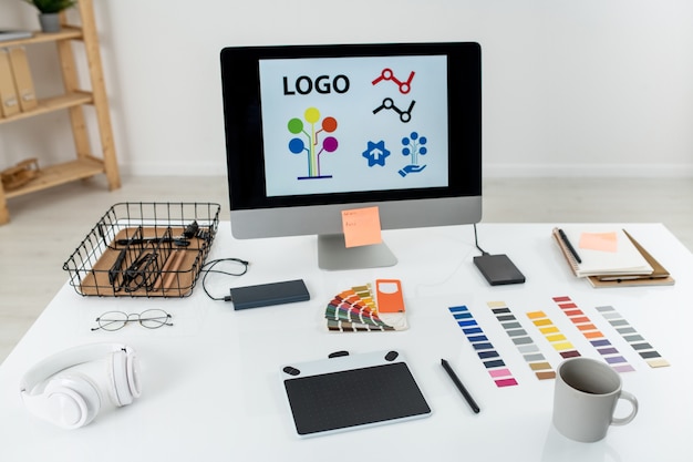 Computermonitor met logo op scherm, grafisch tablet met stylus, mok, palet en andere dingen op bureau