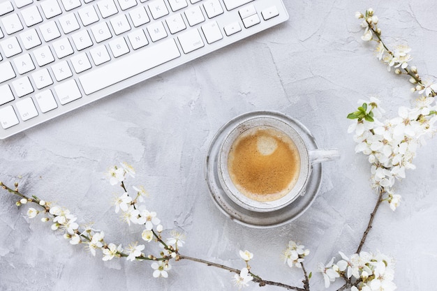 Computertoetsenbord op lente grijze achtergrond met witte kersenbloesem bloemen en ochtend espresso koffie kopie ruimte