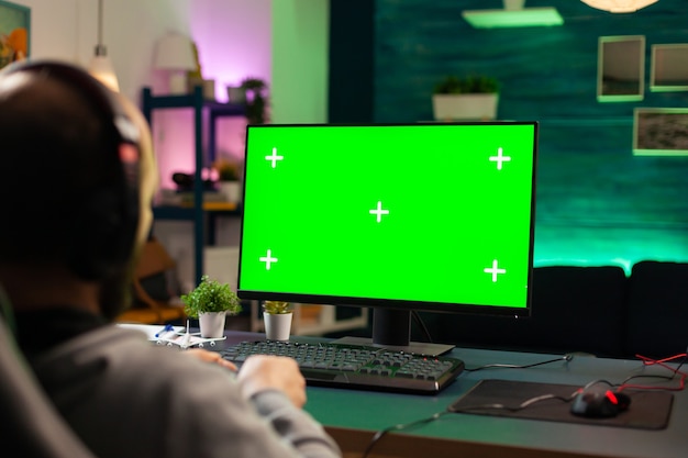 Concentrati sul giocatore che gioca su un computer potente con un mock up verde durante lo streaming della competizione online. giocatore che utilizza un pc con giochi sparatutto in streaming desktop isolati con schermo verde che indossano l'auricolare