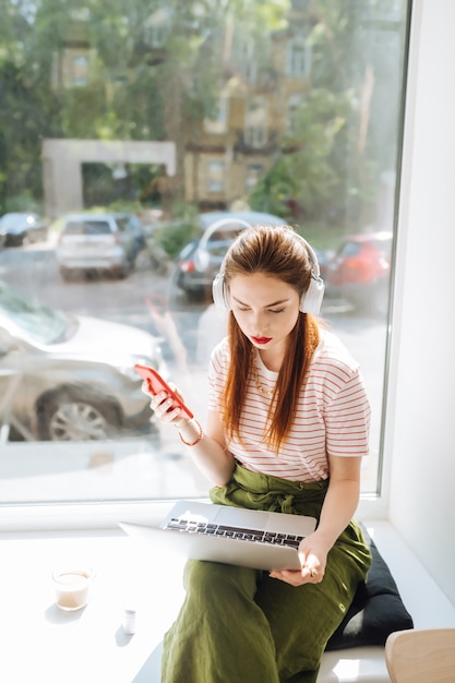 Concentrate on task. Longhaired girl wearing headphones while watching video on laptop