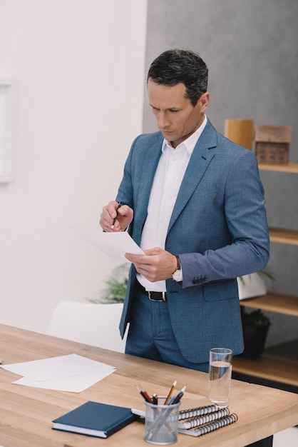 Концентрированный взрослый бизнесмен, читающий деловую бумагу в офисе