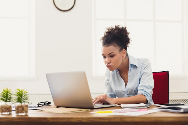 Concentrated african-american business woman working on laptop at office. Businesswoman typing something on computer, sitting at her working place, copy space, side view