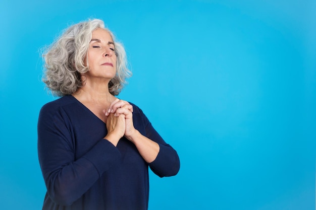 Concentrated aged woman praying with the eyes closed