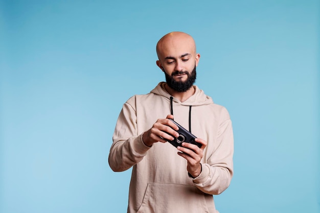 Concentrated arab man playing online game on smartphone. Young carefree bald bearded gamer enjoying leisure time and having fun while using videogame application on mobile phone