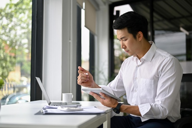 Концентрированный азиатский бизнесмен, управляющий своей работой на цифровом планшете