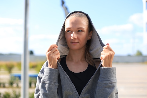 Concentrated athletic caucasian woman with a hood on her head wearing gray hoodie looking to the camera.