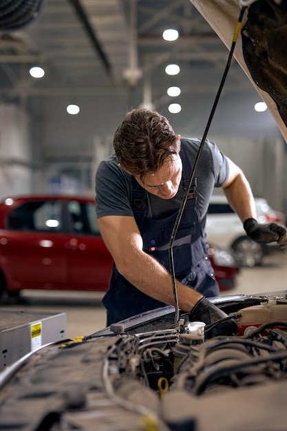 Photo concentrated auto mechanic male working alone repairing engine of the car in hood looking at details...