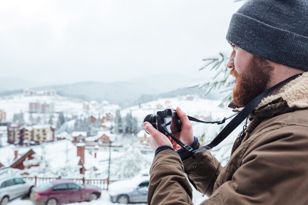 Concentrated bearded young man taking pictures of view outdoors in winter