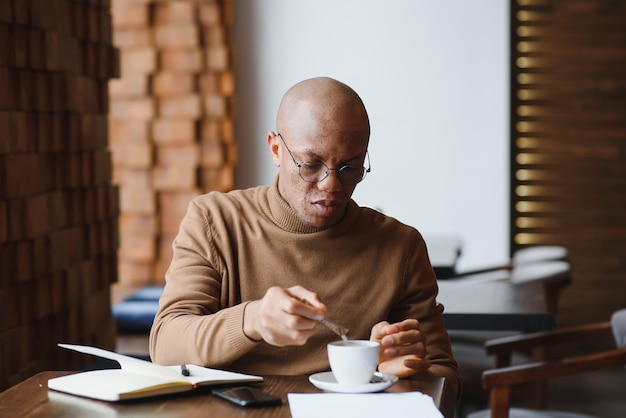 Concentrated black male entrepreneur reads paper documents sitting in cafe with coffee near window.