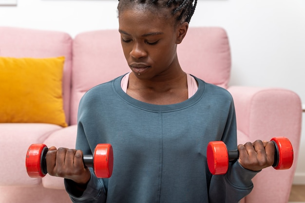 Concentrated black sportswoman exercising with dumbbells on mat during workout at home
