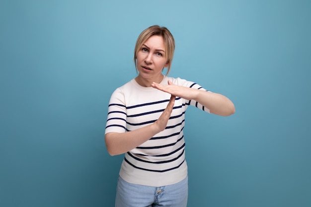 Concentrated blond girl shows hand gesture letter t on blue background with copy space