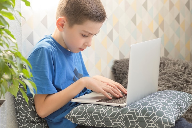 Concentrated boy sitting at desk with laptop computer and doing homework.