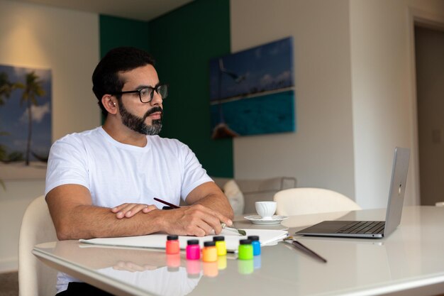 Concentrated brunette man painting small canvas with brush and colored paints