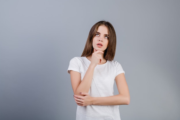 Concentrated brunette woman thinking looking at copyspace isolated over grey