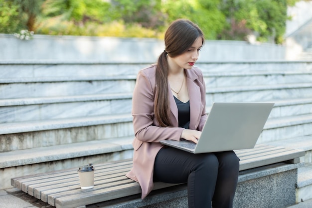 Concentrated business woman using laptop while sitting on a bench in the park