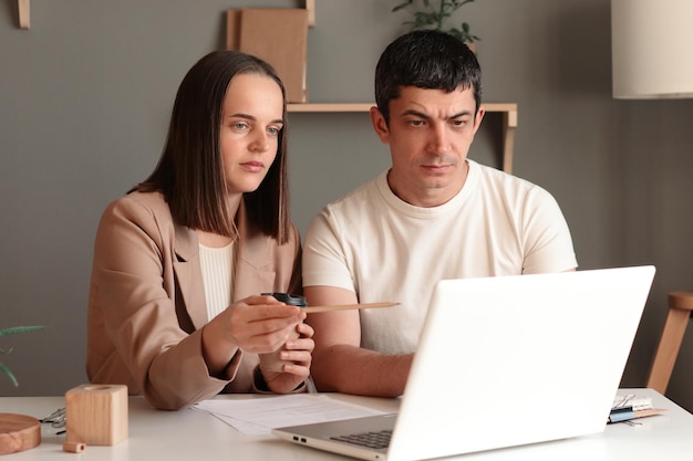 Concentrated businessman looking at computer monitor working with a young female worker on a project people using notebook sitting at table in office