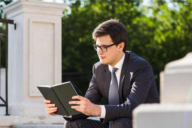 Сконцентрированный бизнесмен читает книгу снаружи