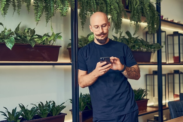 Concentrated businessman uses smartphone with headphones while stands in home office distance job