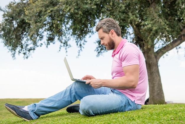 Concentrated businessman using laptop for blogging on green grass work online