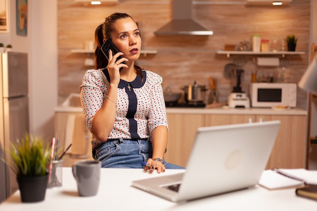 Concentrated businesswoman during phone call late at night from home office. Employee using modern technology at midnight doing overtime for job, business, busy, career, network, lifestyle ,wireless.