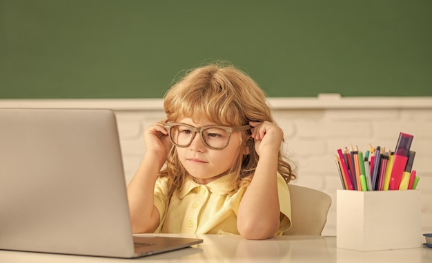안경을 쓴 집중된 소년은 컴퓨터 교육을 통해 학교 교실에서 온라인으로 공부합니다.