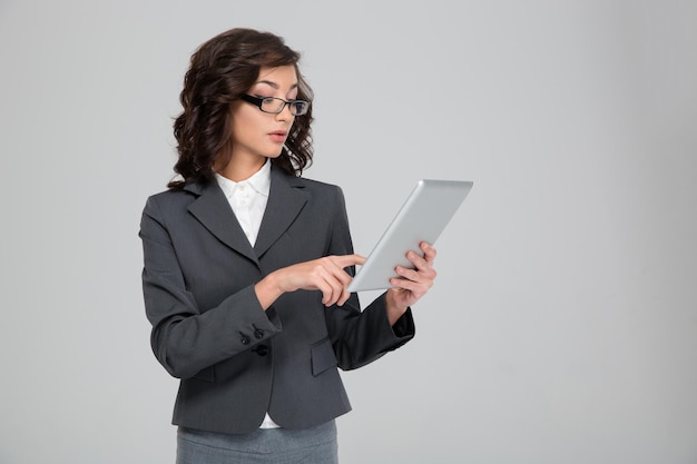 Concentrated confident pretty young business woman in glasses using tablet