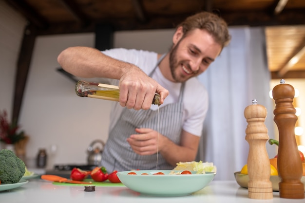 Un cuoco concentrato che mette un po 'd'olio in un'insalata