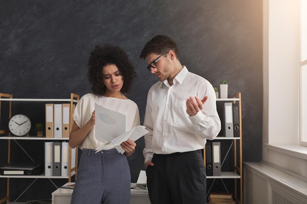 Concentrated couple of young colleagues working in modern office. Two coworkers discussing their work, working with documents. Businesswoman pointing on paper, copy space