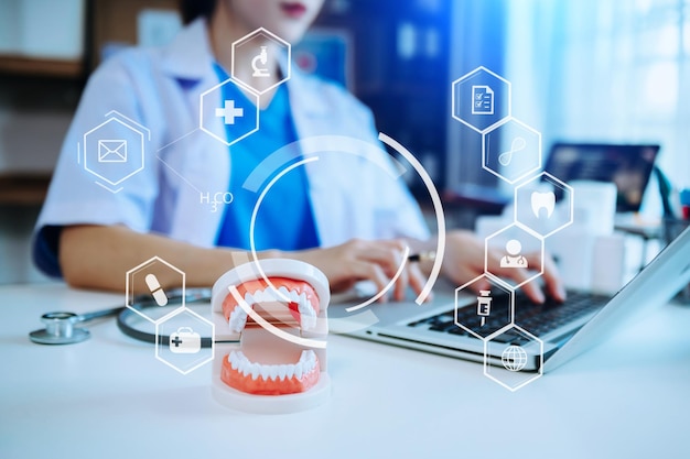 Photo concentrated dentist sitting at table with jaw samples tooth model and working with tablet and laptop in dental office professional dental clinic with virtual icon hologram