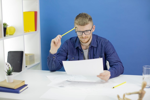 Concentrated designer looking on pencil sketches layout holding pencil at temple