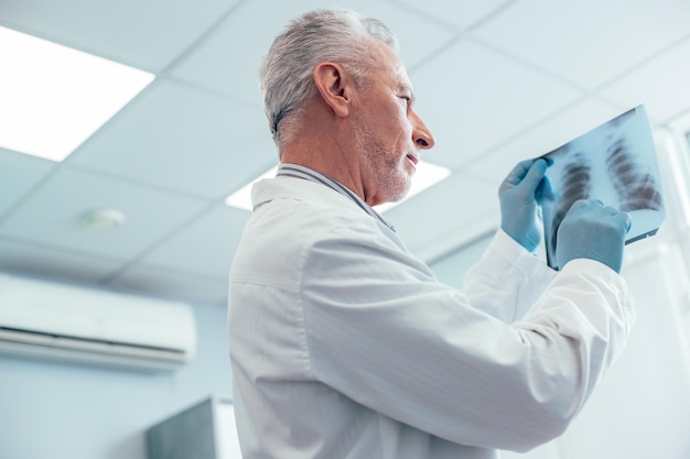 Medico di famiglia concentrato che pone la diagnosi di polmonite mentre guarda la radiografia del torace