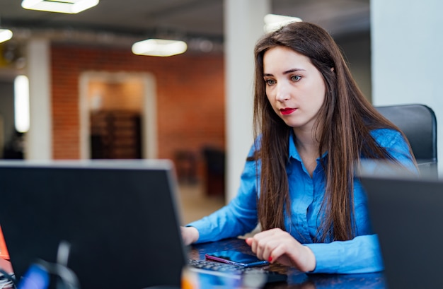 집중된 여성 개발자는 현대 사무실의 컴퓨터에서 작업하고 있습니다. 매력적인 젊은 여성 프로그래머는 IT 회사에서 새로운 기술을 개발하고 있습니다. 고품질 이미지.