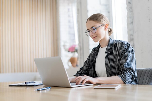 Concentrated female professional in glasses and plaid jacket typing on laptop office setting with