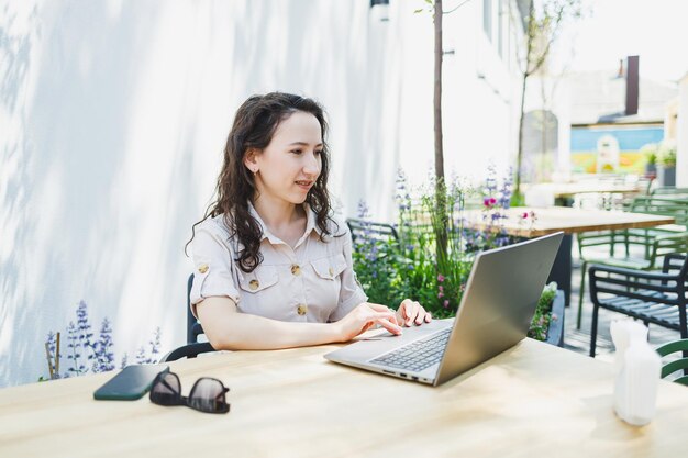 Concentrated female student writing on laptop while studying with cup in cafe thoughtful freelancer jotting down information for project planning doing remote work via laptop