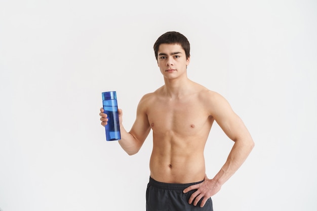 Concentrated fit young shirtless sportsman showing water bottle over white