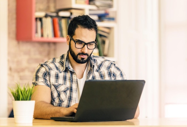 Concentrated freelance worker bearded handsome man working with laptop in modern coworking office