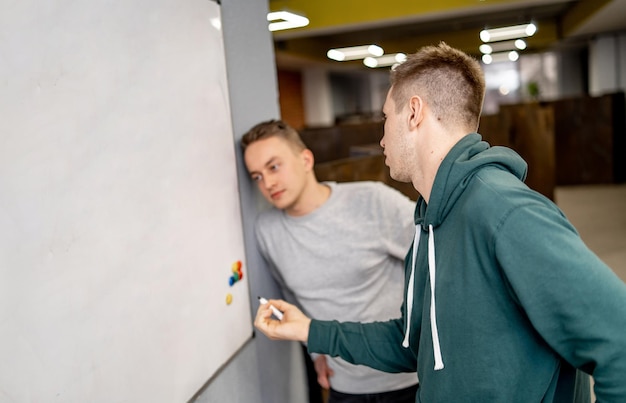 Concentrated guys standing near whiteboard. Writing or solving equations in modern hall.