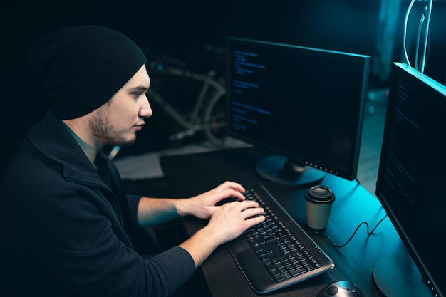 Concentrated hacker in sweatshirt and cap breaks into corporate servers from his underground hideout