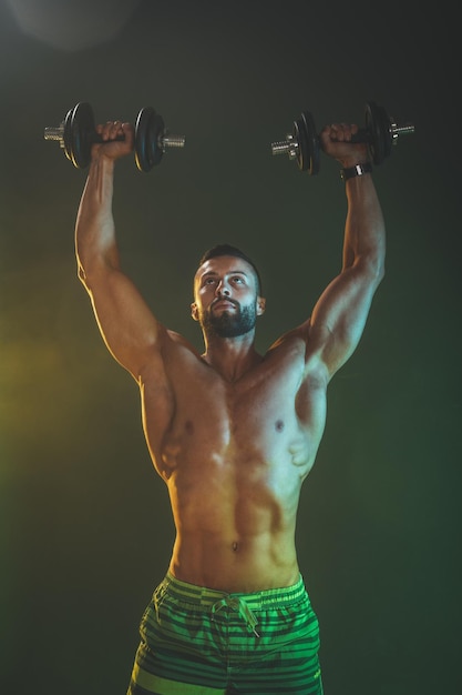 Concentrated handsome muscular man is training actively and hard with dumbbells.