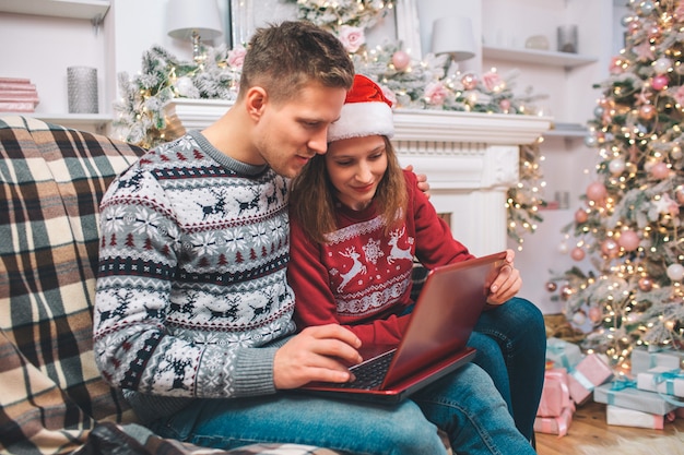 Concentrated and interested young man and woman works using laptop. They look at it. Guy pushes buttons. They wear festive clothes.