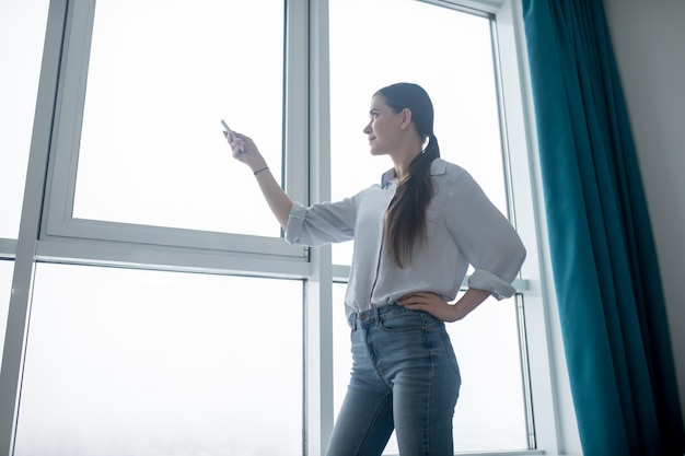 Concentrated lady using a remote control for closing the blinds