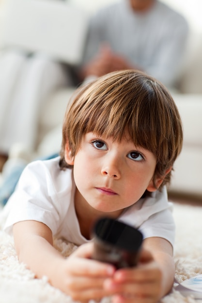 Concentrated little boy watching TV lying on the floor 