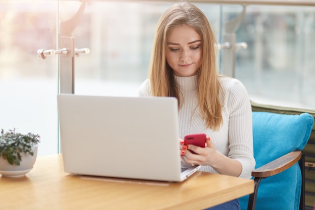 Ragazza bionda dai capelli lunghi concentrata dello studente che controlla rete sociale con il telefono mentre avendo resto in caffè.