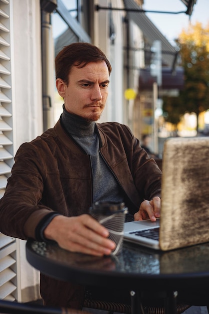 Concentrated male freelancer with cup of coffee using laptop while working on remote project in cafe