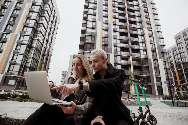 L'uomo concentrato aiuta la sua ragazza con il problema del computer portatile. giovani coppie che si siedono fuori e che lavorano al computer portatile. sono venuti qui con gli scooter. concetto di trasporto ecologico.